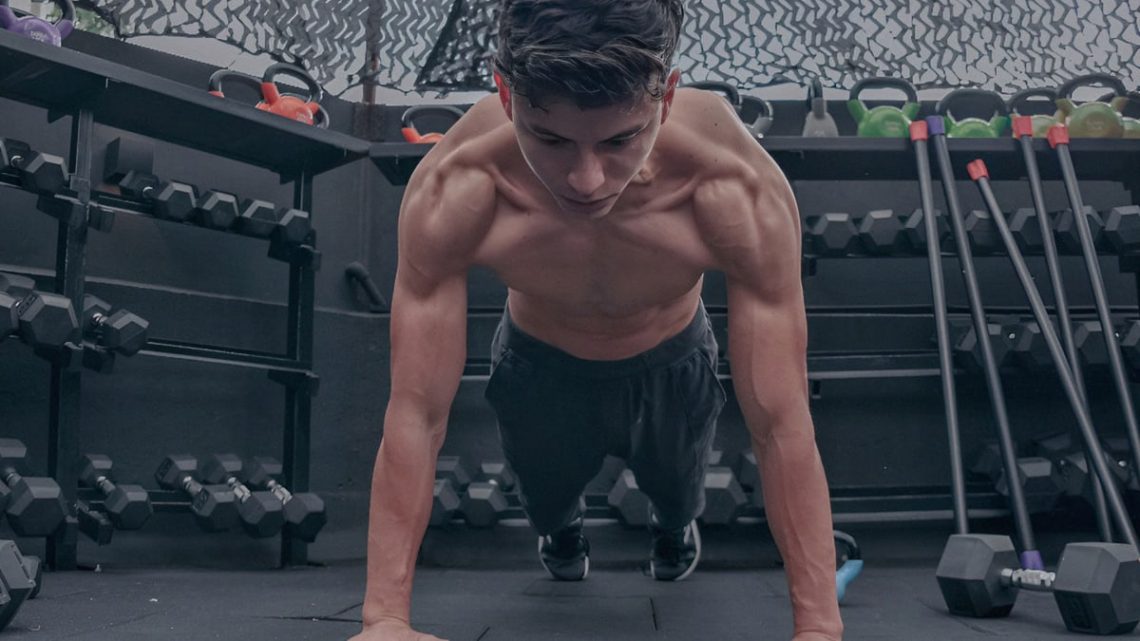 A muscular young man doing push ups in a modern gym setting